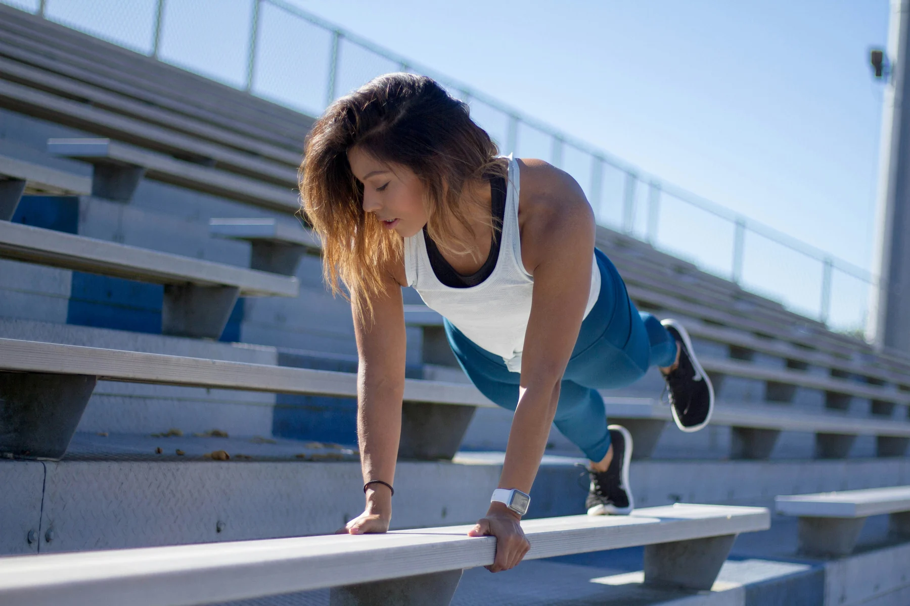 Woman doing a plank on stadium bleachers on a sunny day